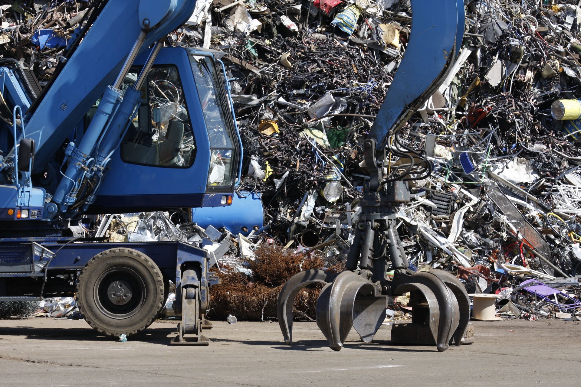 A blue recycling truck is parked in a yard, surrounded by scrap metal. A blue recycling truck is parked in a yard, surrounded by scrap metal.