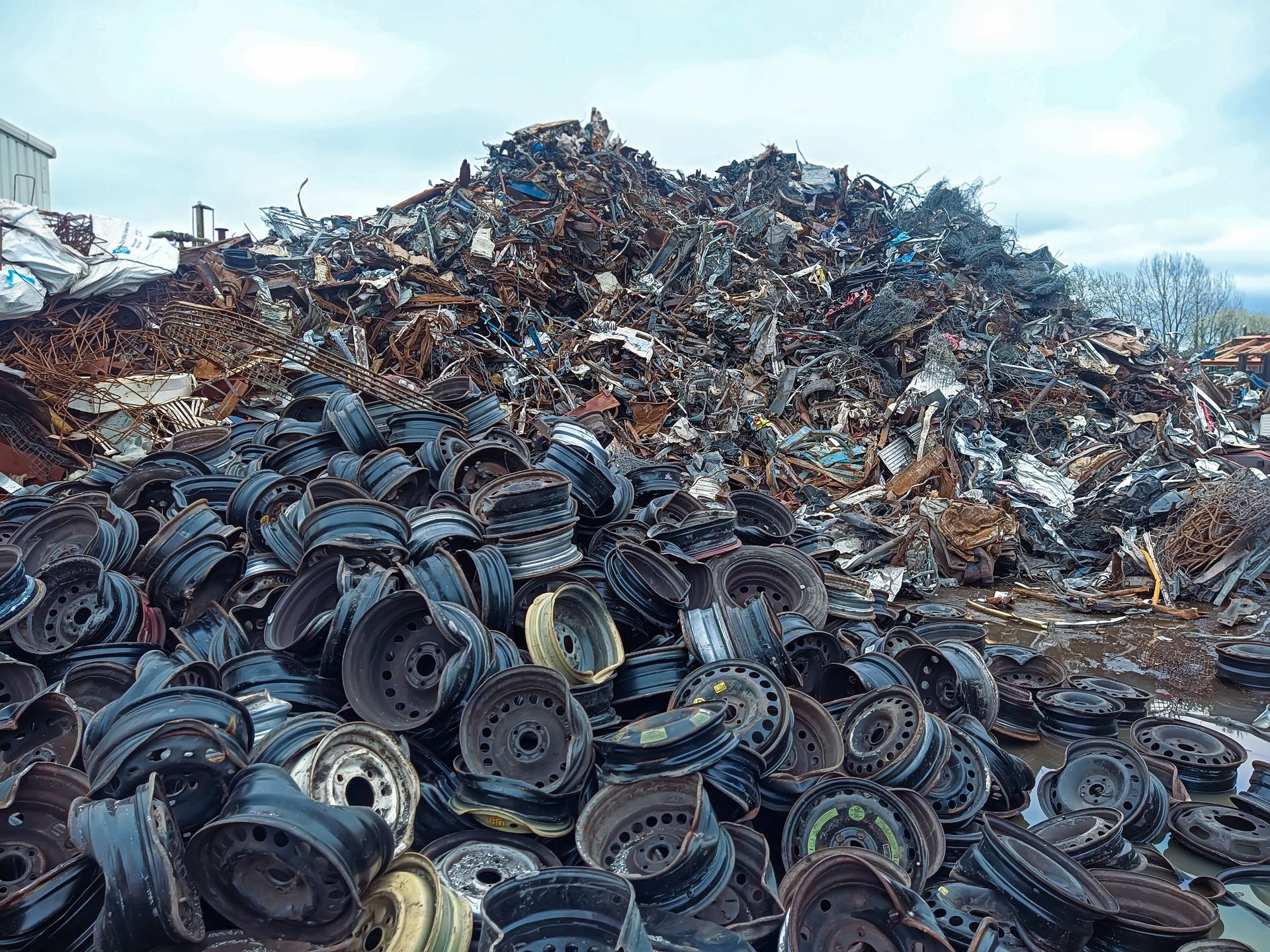 A blue recycling truck is parked in a yard, surrounded by scrap metal. A blue recycling truck is parked in a yard, surrounded by scrap metal.