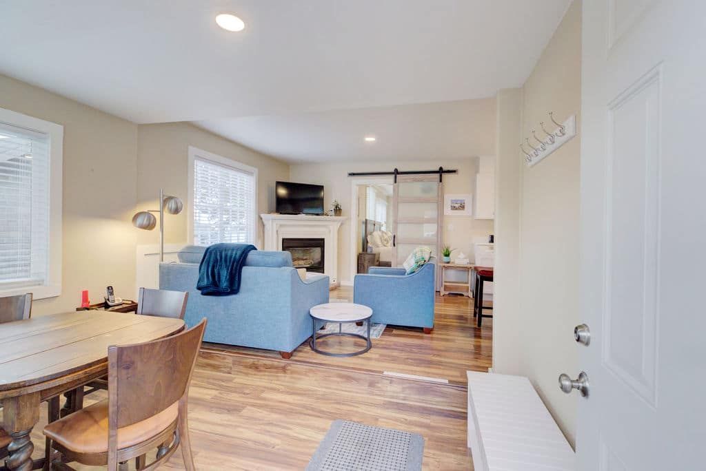 Living room with blue sofas, fireplace, round dining table, and open entry door.