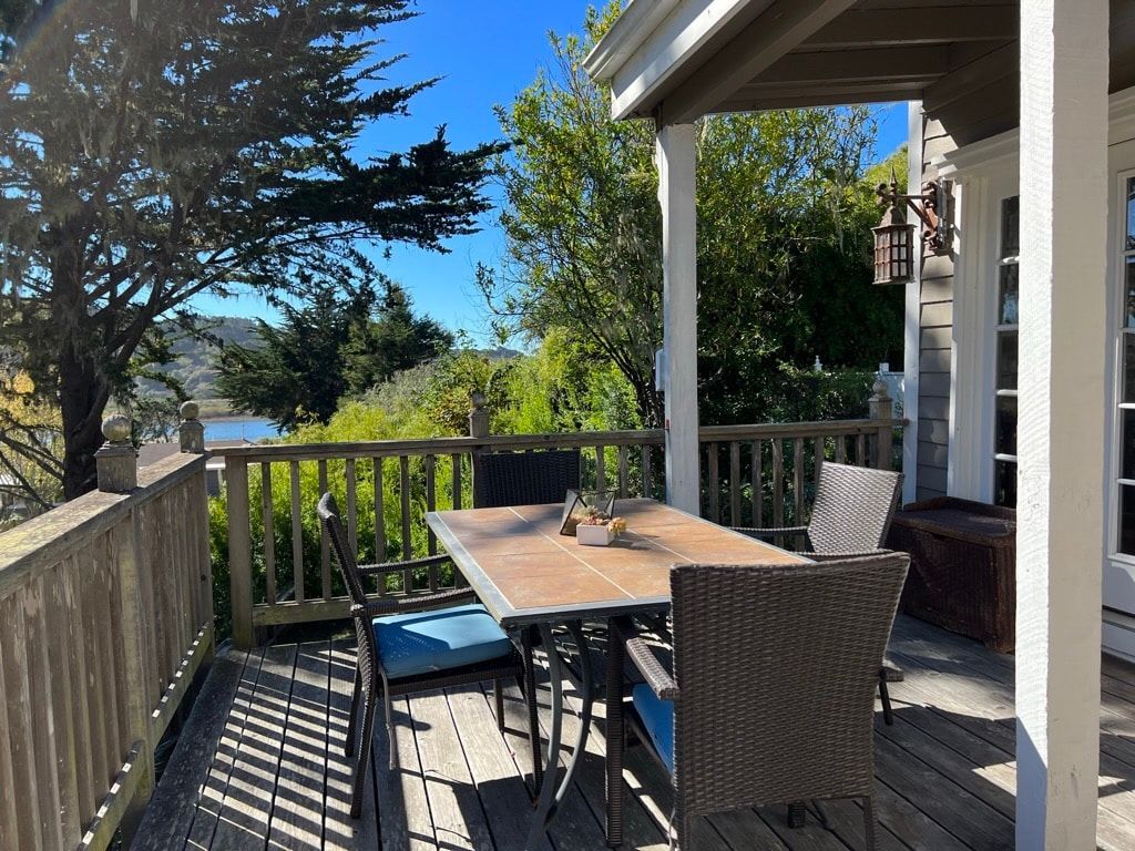 Wooden deck with table and chairs overlooking water and trees on a sunny day.