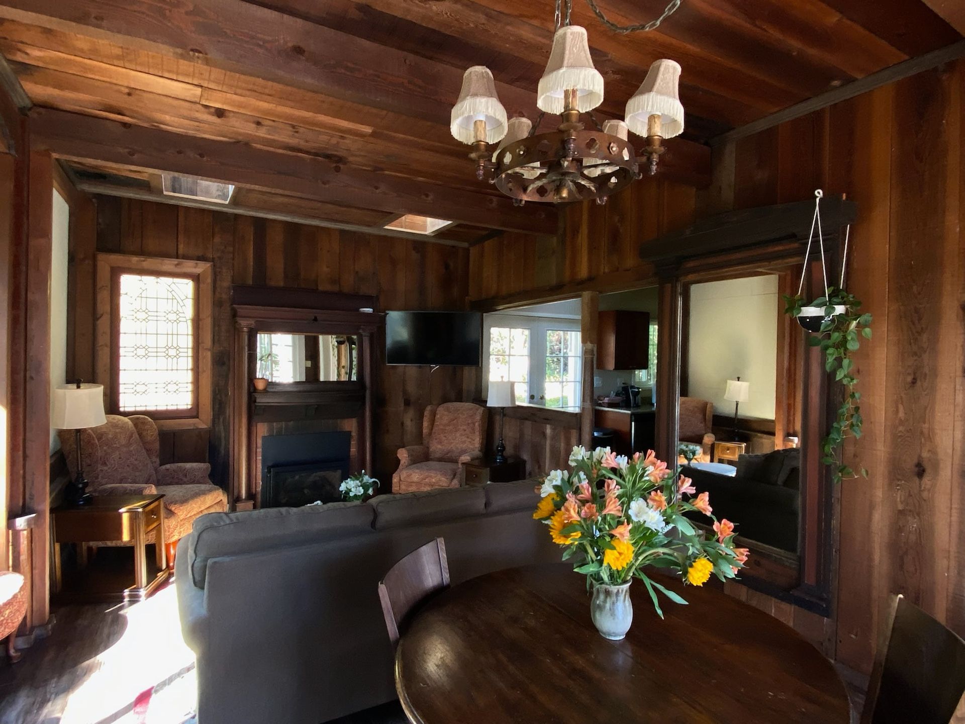 Cozy living room with dark wood paneling, a chandelier, and a round table with flowers.