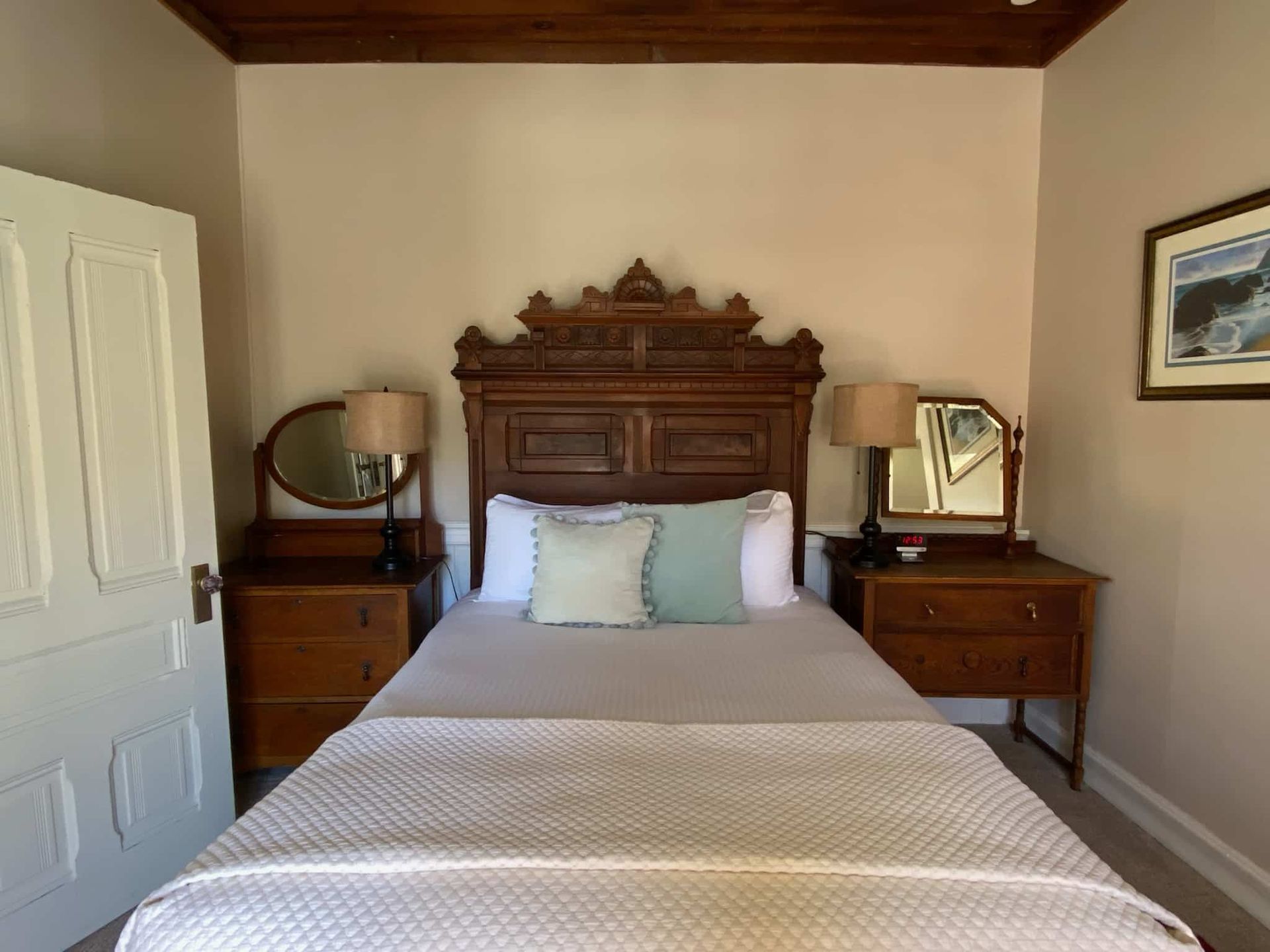 Bedroom with antique wooden bed, nightstands, and wall art. Soft colors.