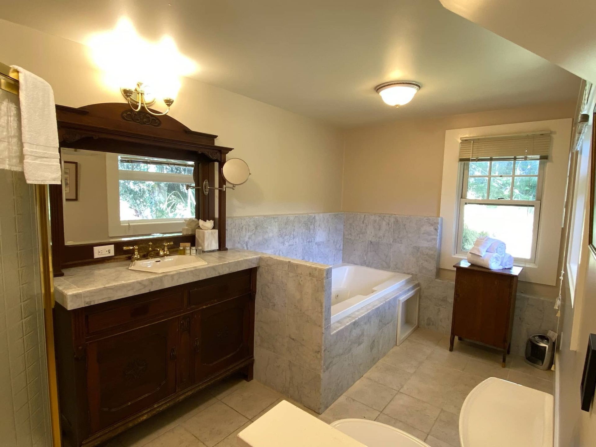 Bathroom with dark wood vanity, marble tub surround, and small window.