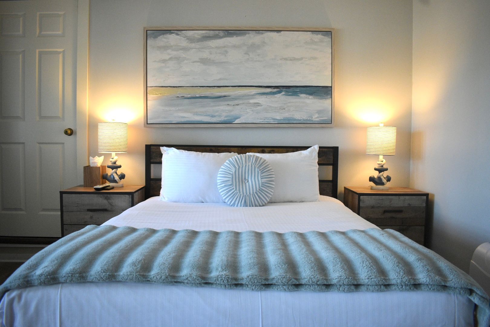Bedroom with blue bedding, tan walls, wooden nightstands, and wall art.