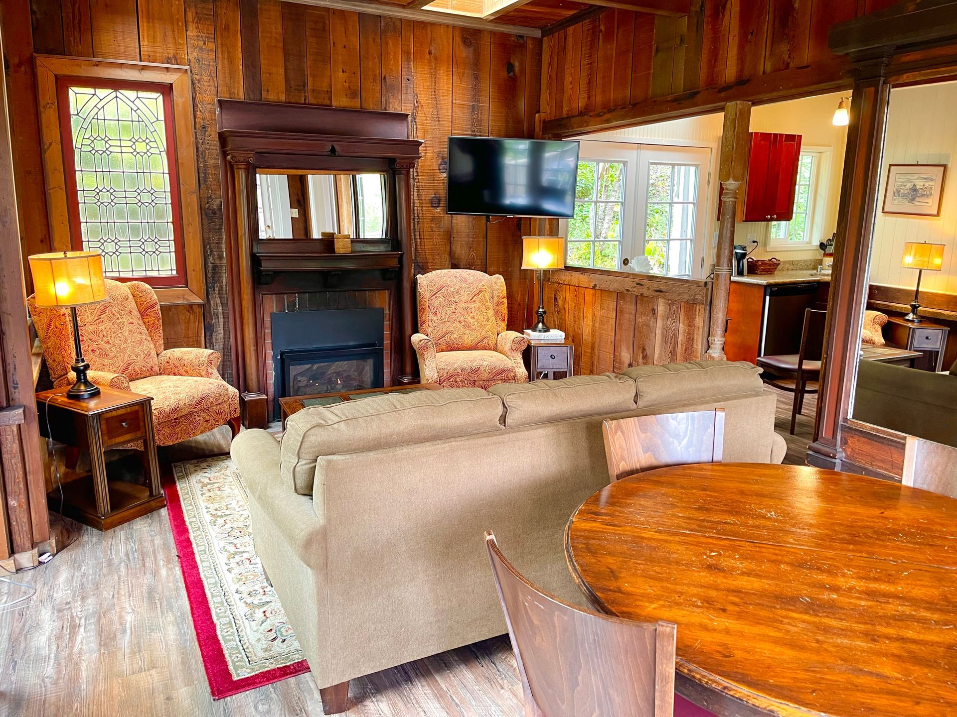 Cozy living room with wood paneling, fireplace, and two armchairs; a couch, and a small TV.