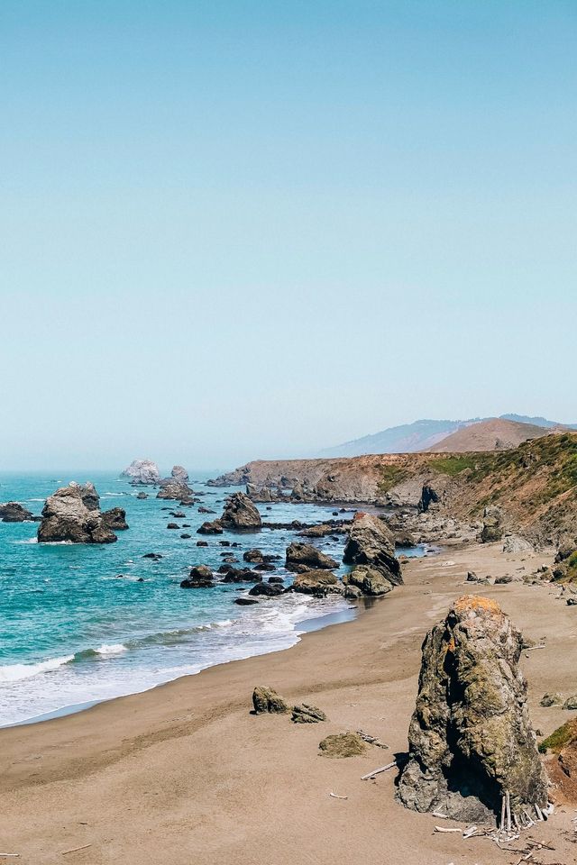 Sandy beach and turquoise water along a rocky coastline, under a blue sky.
