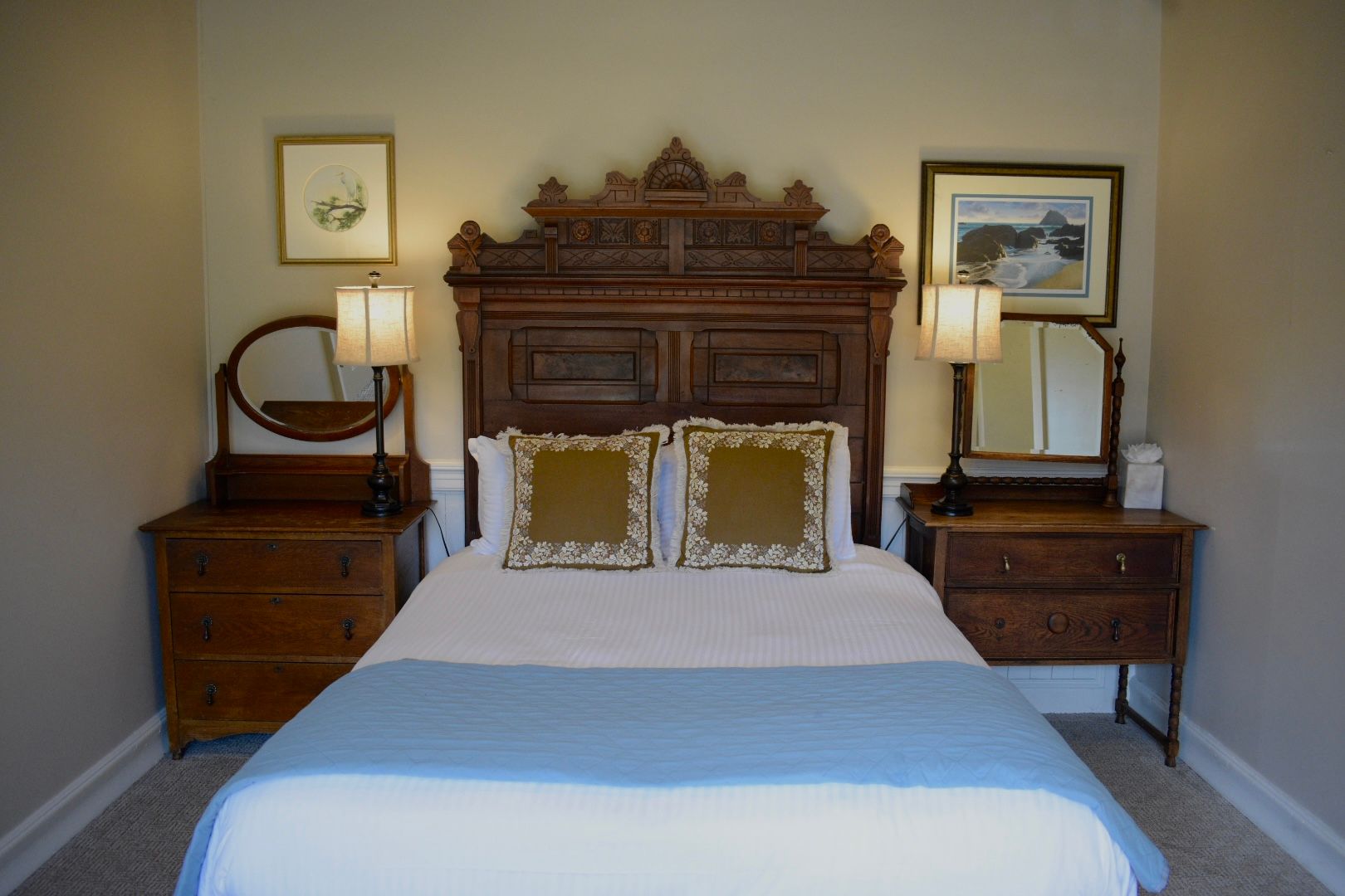 Bedroom with antique wooden bed, nightstands, and wall art. Soft colors.