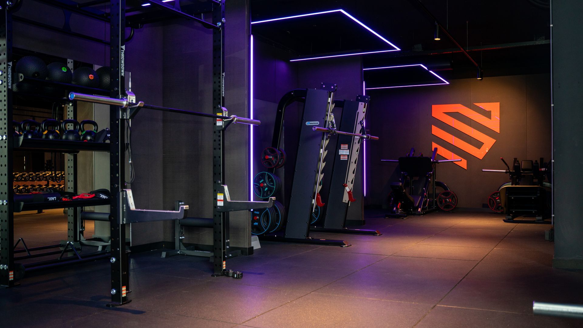 Een man tilt een gewichtsschijf op een halter in de sportschool, met andere mensen op de achtergrond die aan het trainen zijn.