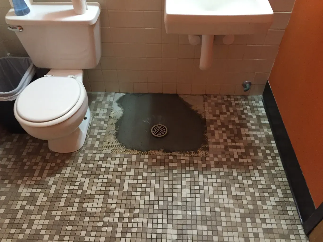 A bathroom with a toilet and sink and a drain on the floor