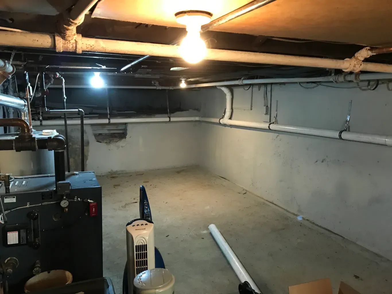 An empty basement with pipes and a light on the ceiling.