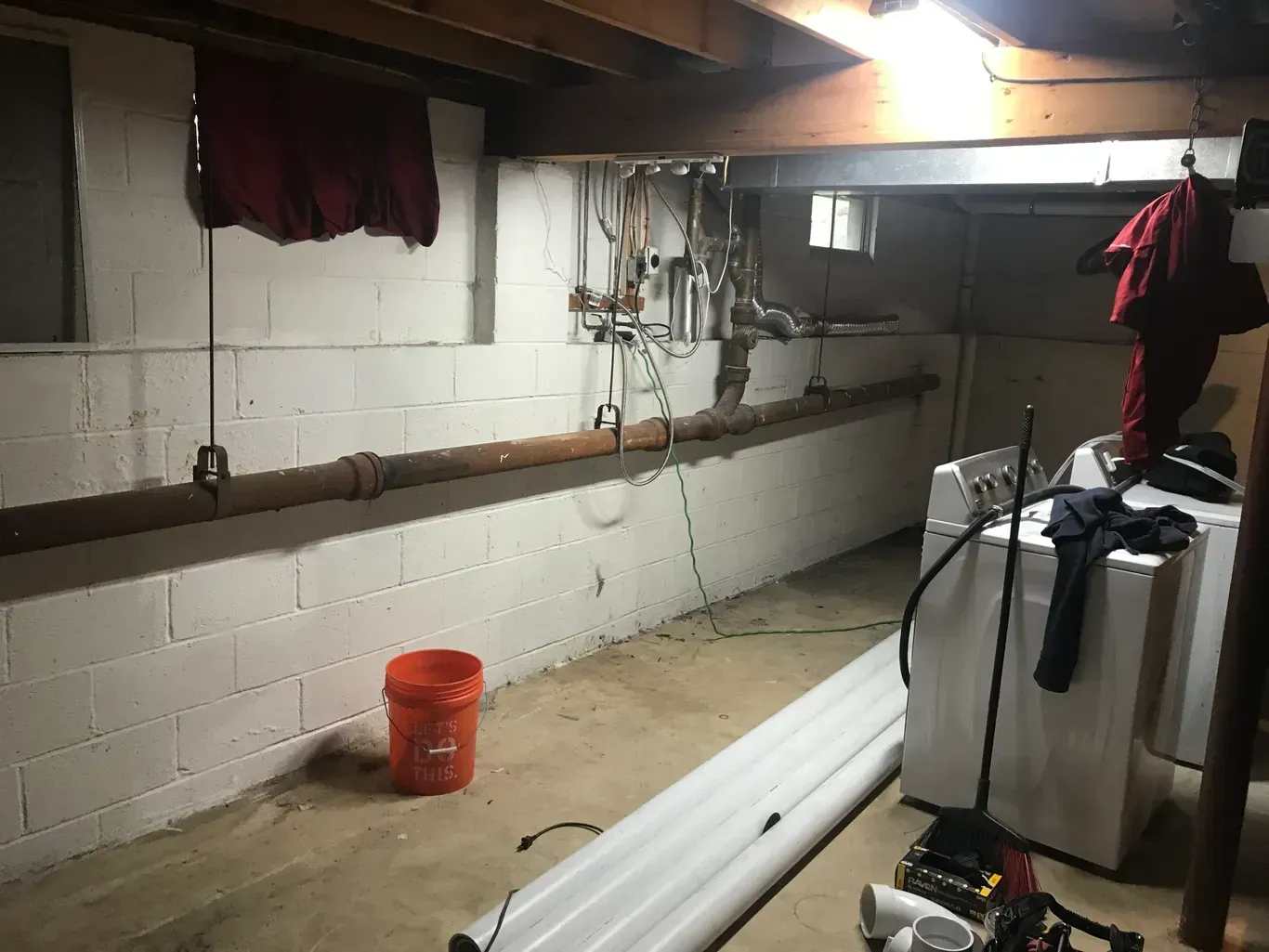 A basement with a washer and dryer and a bucket.