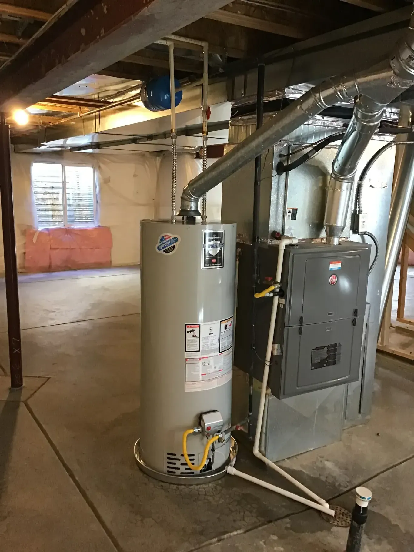A water heater is sitting in a basement next to a furnace.