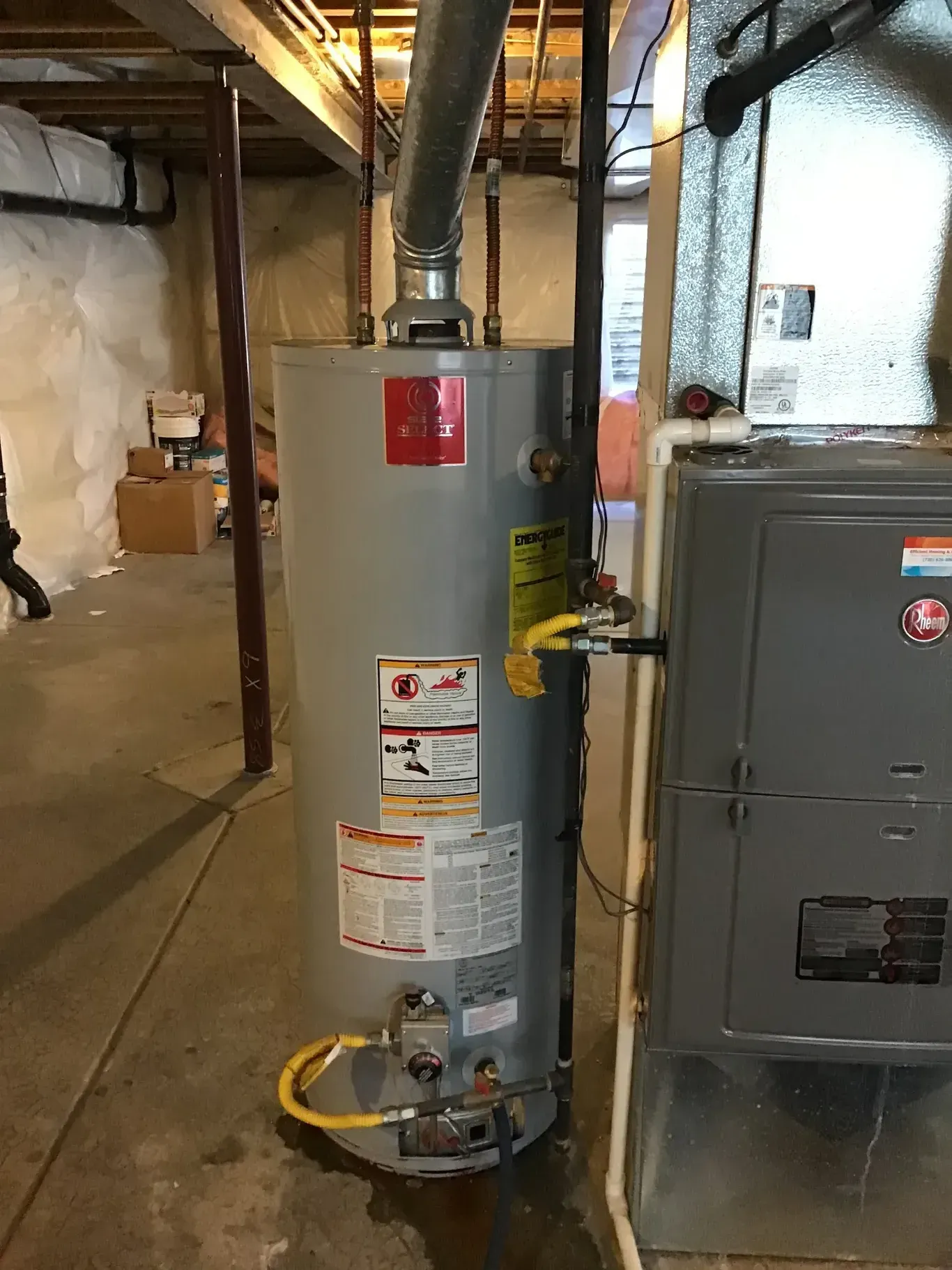 A water heater is sitting next to a furnace in a basement.