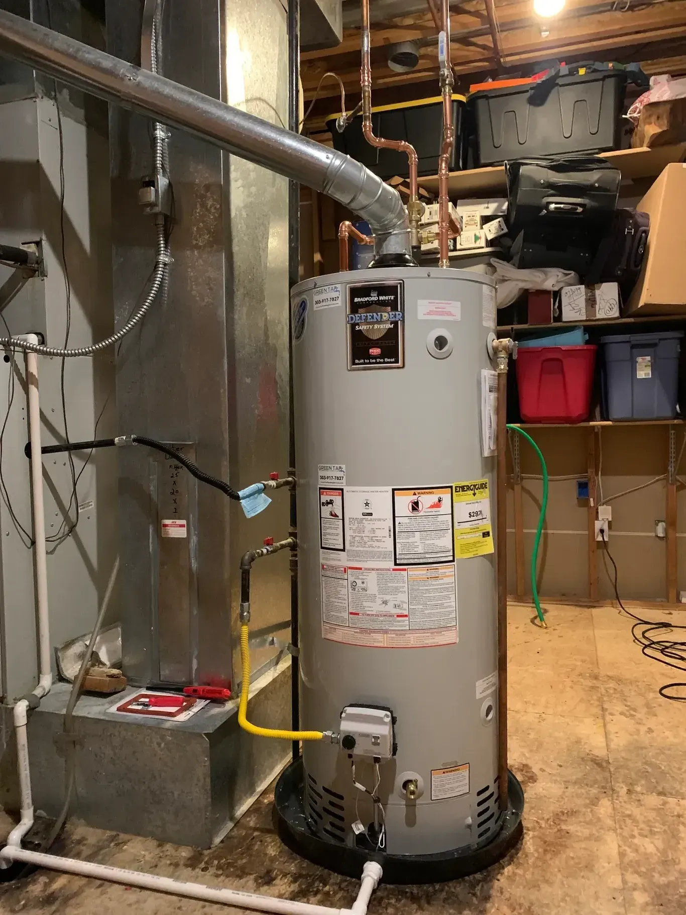 A water heater is sitting in a basement next to a furnace.