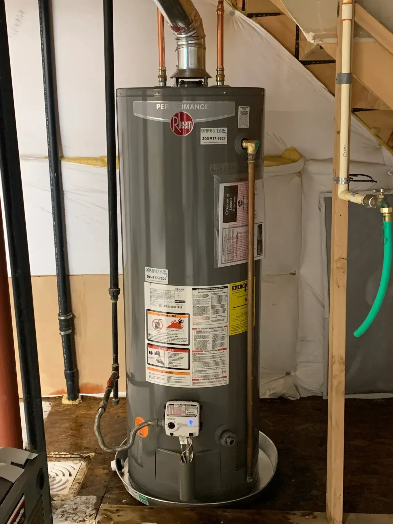 A water heater is sitting in a basement next to a staircase.