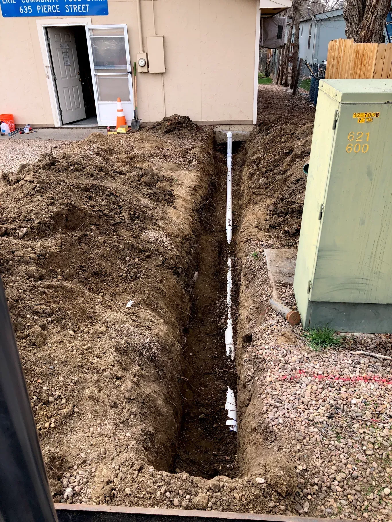 A trench is being dug in the dirt in front of a building.