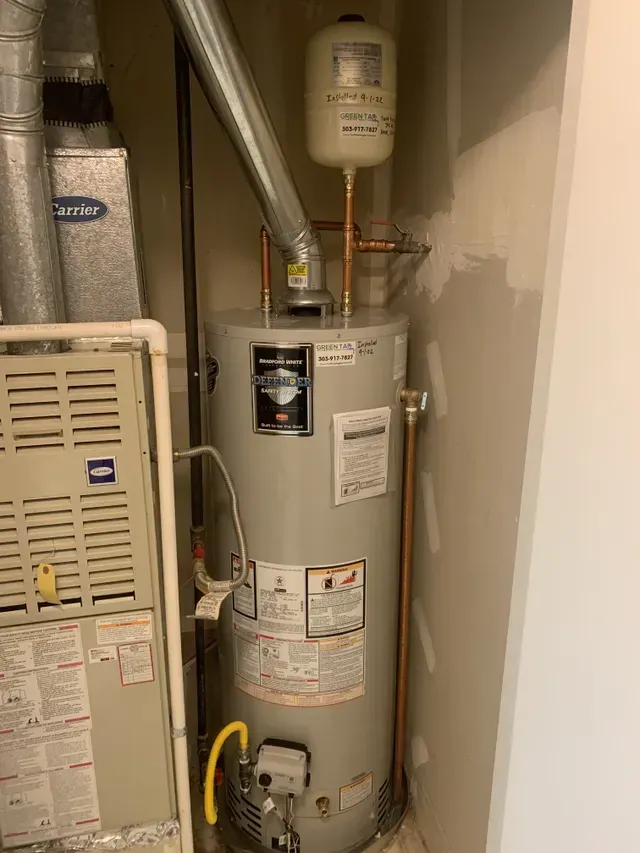 A water heater is sitting in a room next to a furnace.