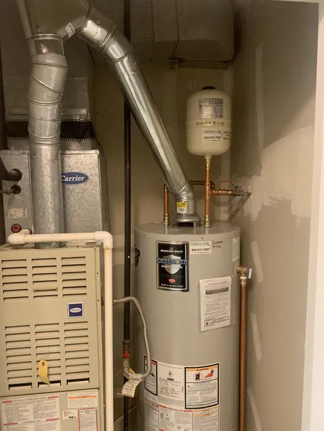 A water heater is sitting next to a furnace in a room.