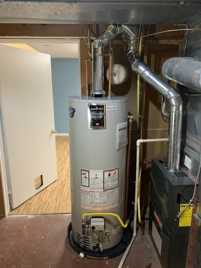 A water heater is sitting in a basement next to a furnace.