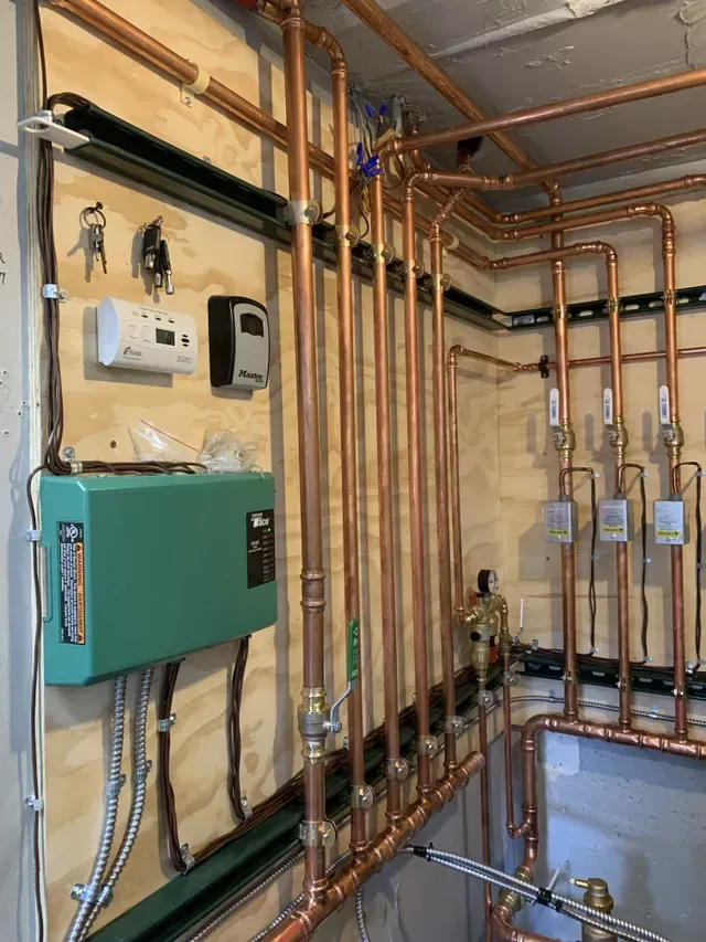 A room with copper pipes and a green box on the wall.