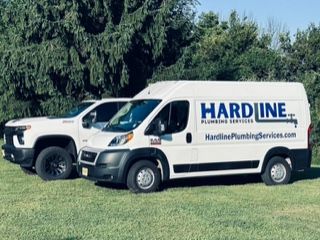 Two hardline plumbing services vans are parked next to each other in a grassy field.