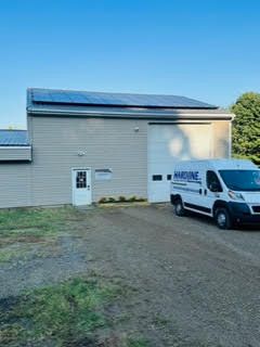 A white van is parked in front of a building with solar panels on the roof.