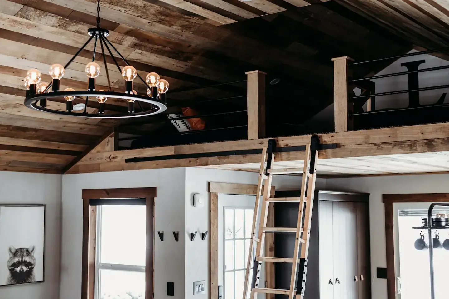 A room with a ladder leading up to a loft and a chandelier hanging from the ceiling.