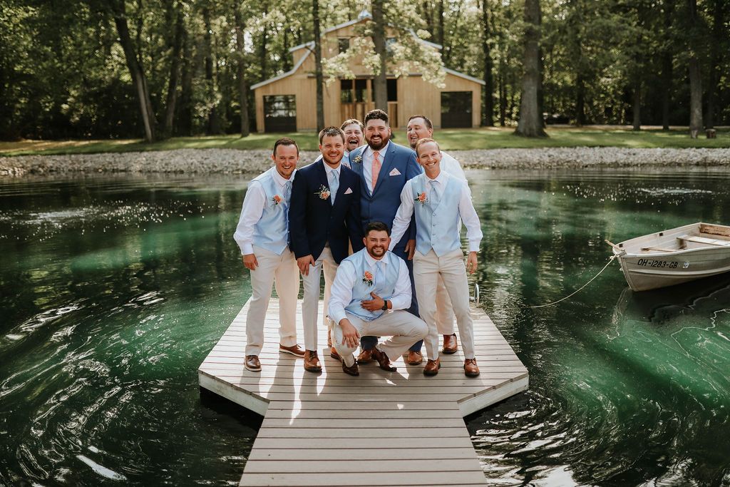 The groom and his groomsmen are posing for a picture on a dock next to a lake.
