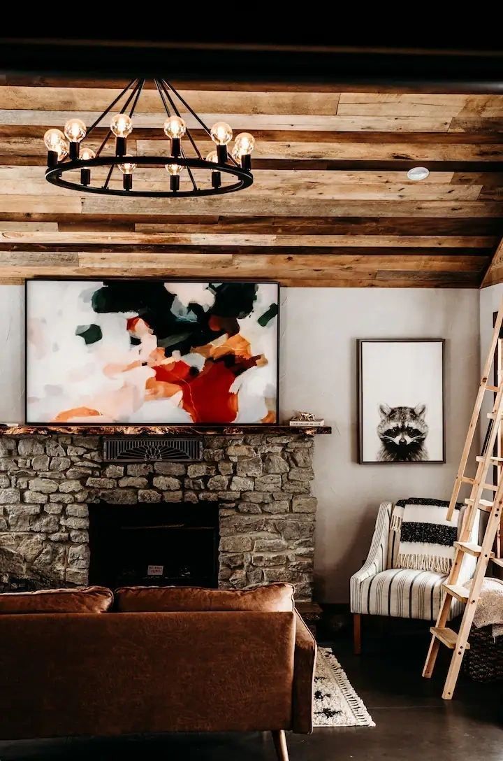 A living room with a stone fireplace , couch , chair , and chandelier.