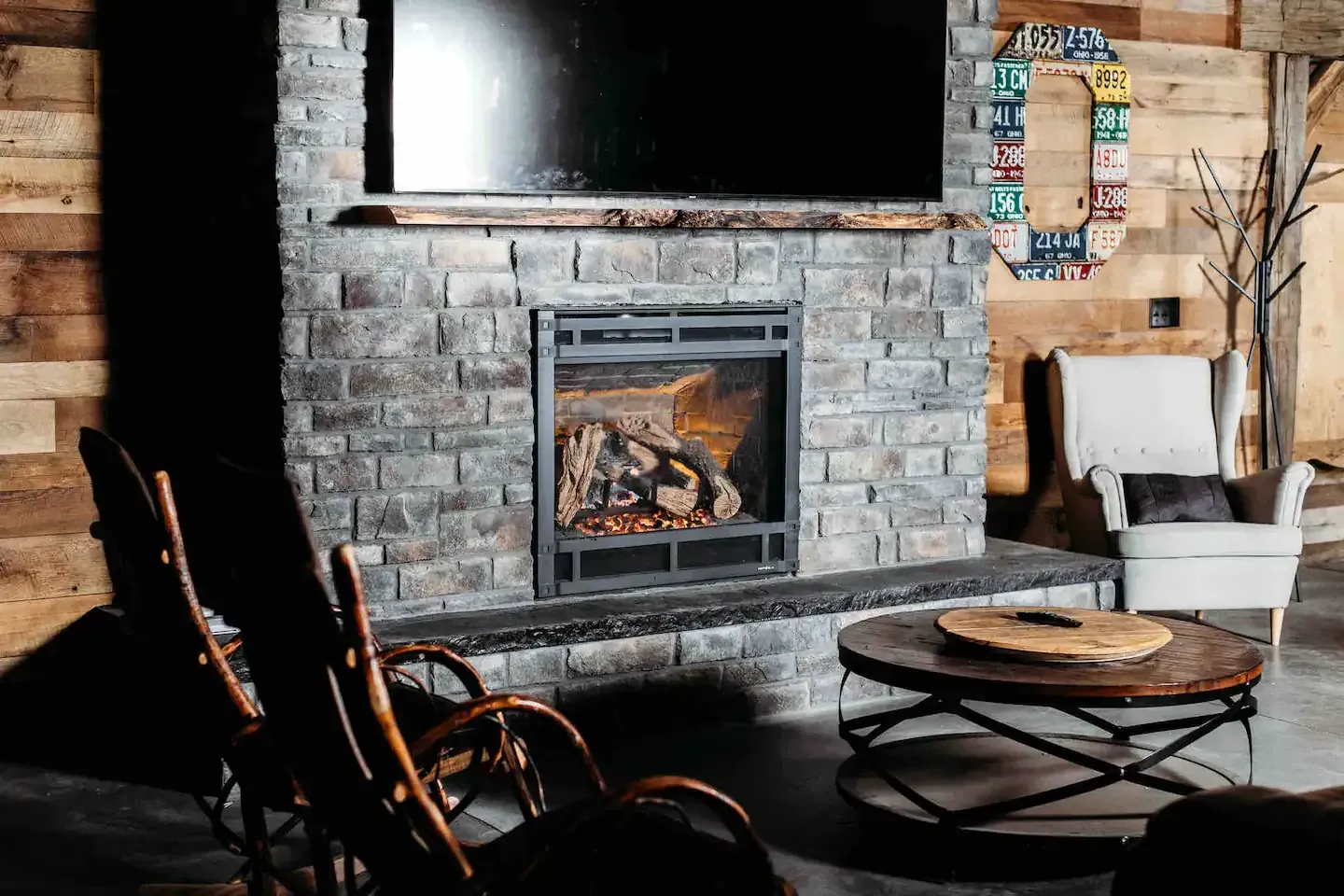 A living room with a fireplace , chairs , a coffee table and a flat screen tv.