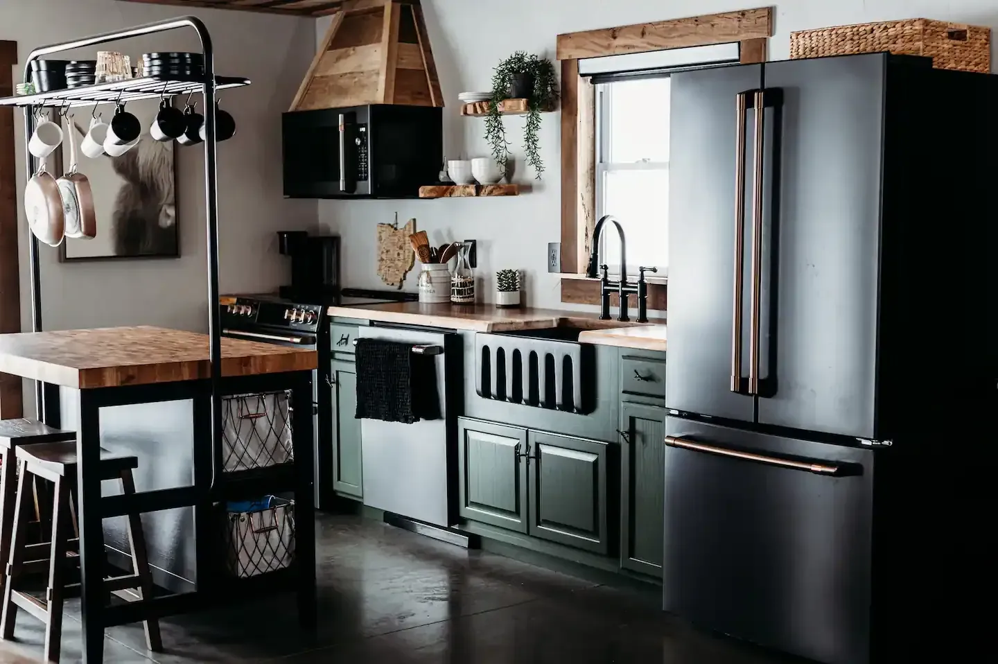 A kitchen with green cabinets , black appliances , and a wooden table.