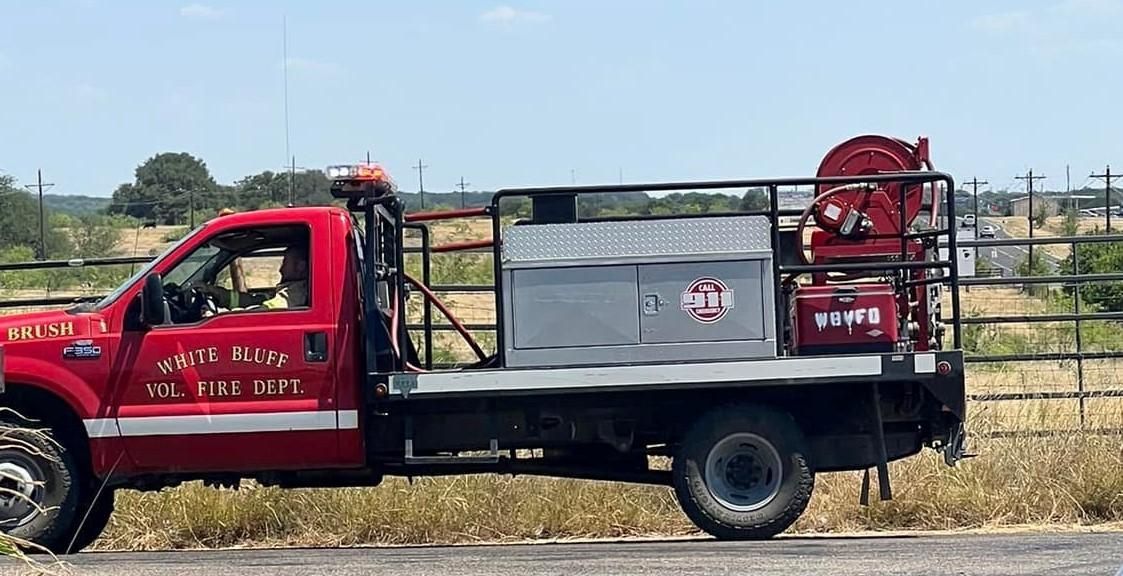 A red truck is parked on the side of the road in a field.