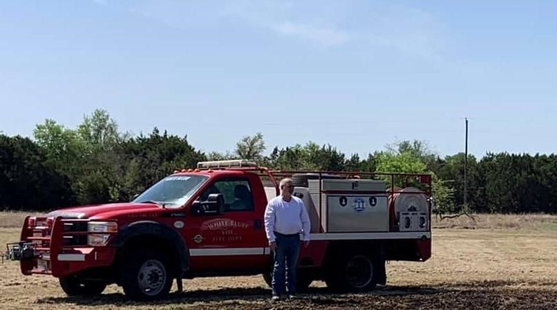 A man is standing next to a red truck in a field.