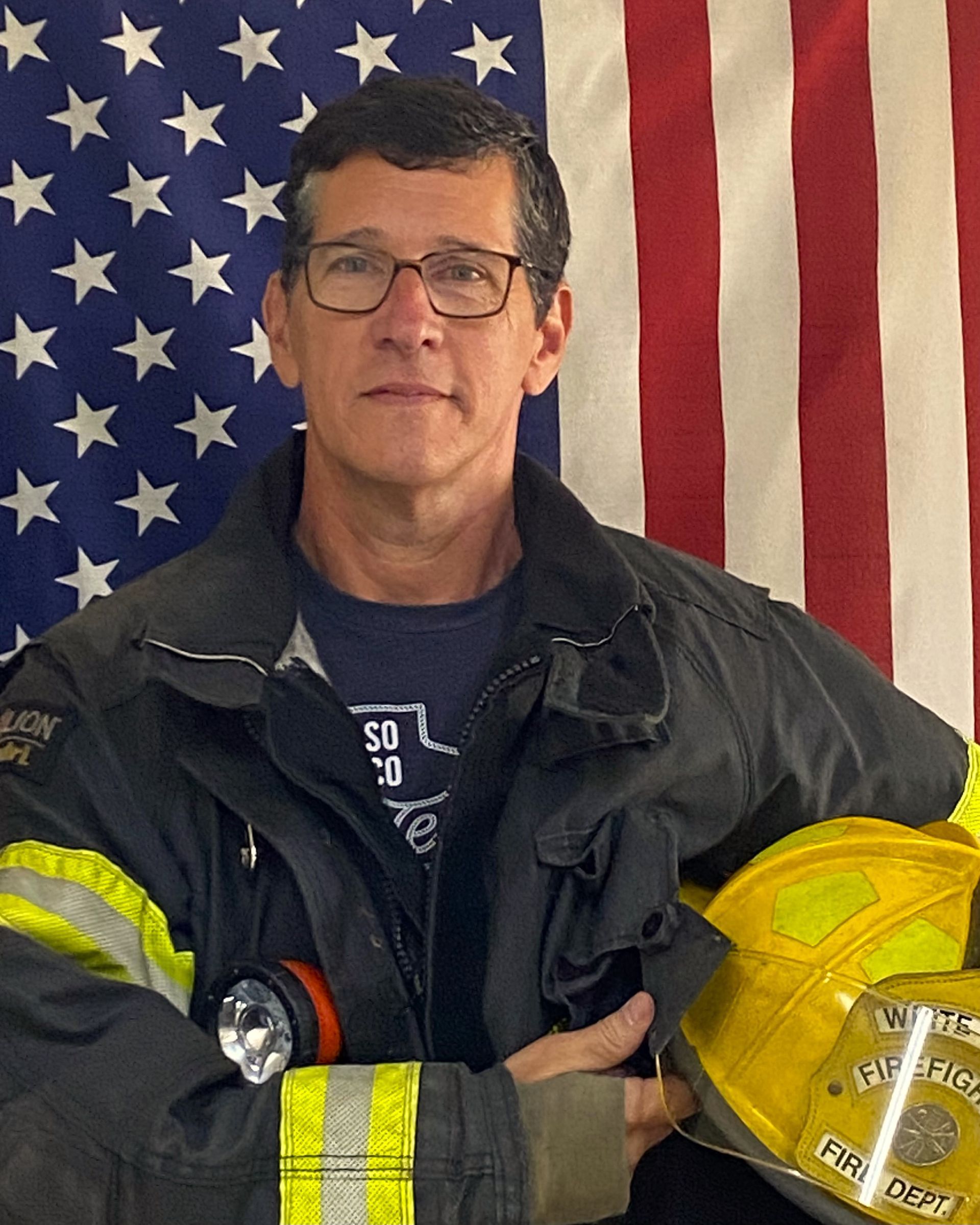 A fireman holding a helmet in front of an american flag