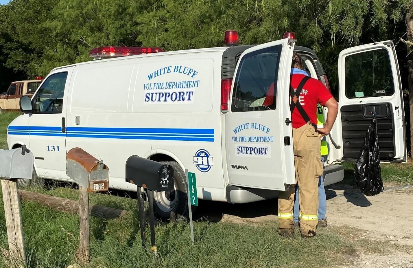 A firefighter is standing next to a white van with the doors open.