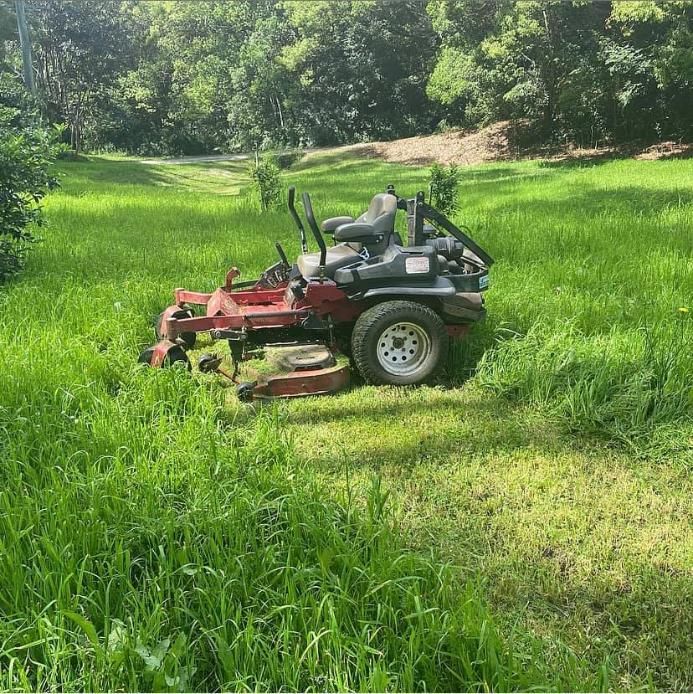 A Red Lawn Mower is Sitting in the Middle of a Lush Green Field — 4WD Slashing & Large Area Mowing In Ballina, NSW