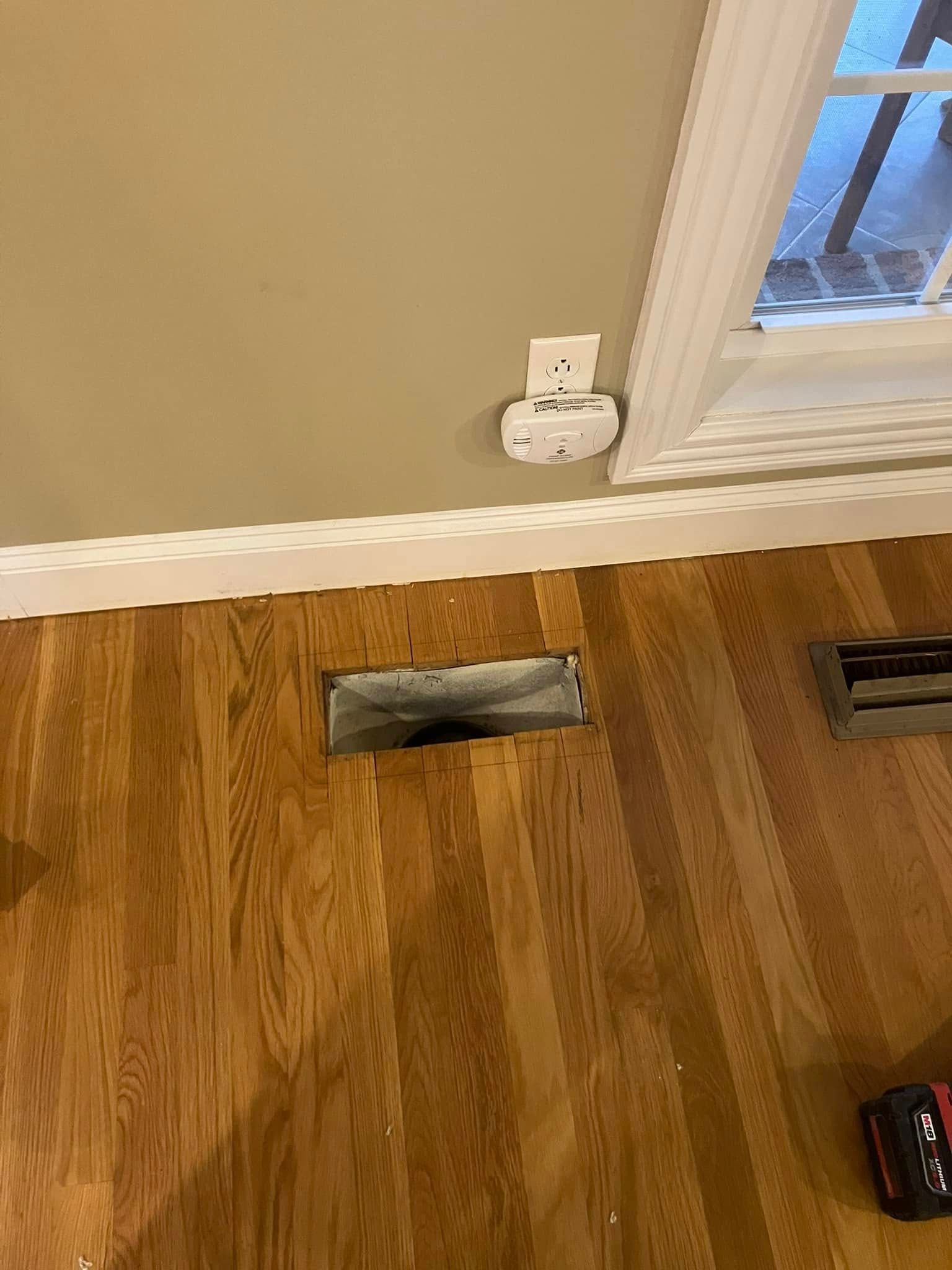 Hardwood floor with two rectangular floor vents beside a white baseboard and window.