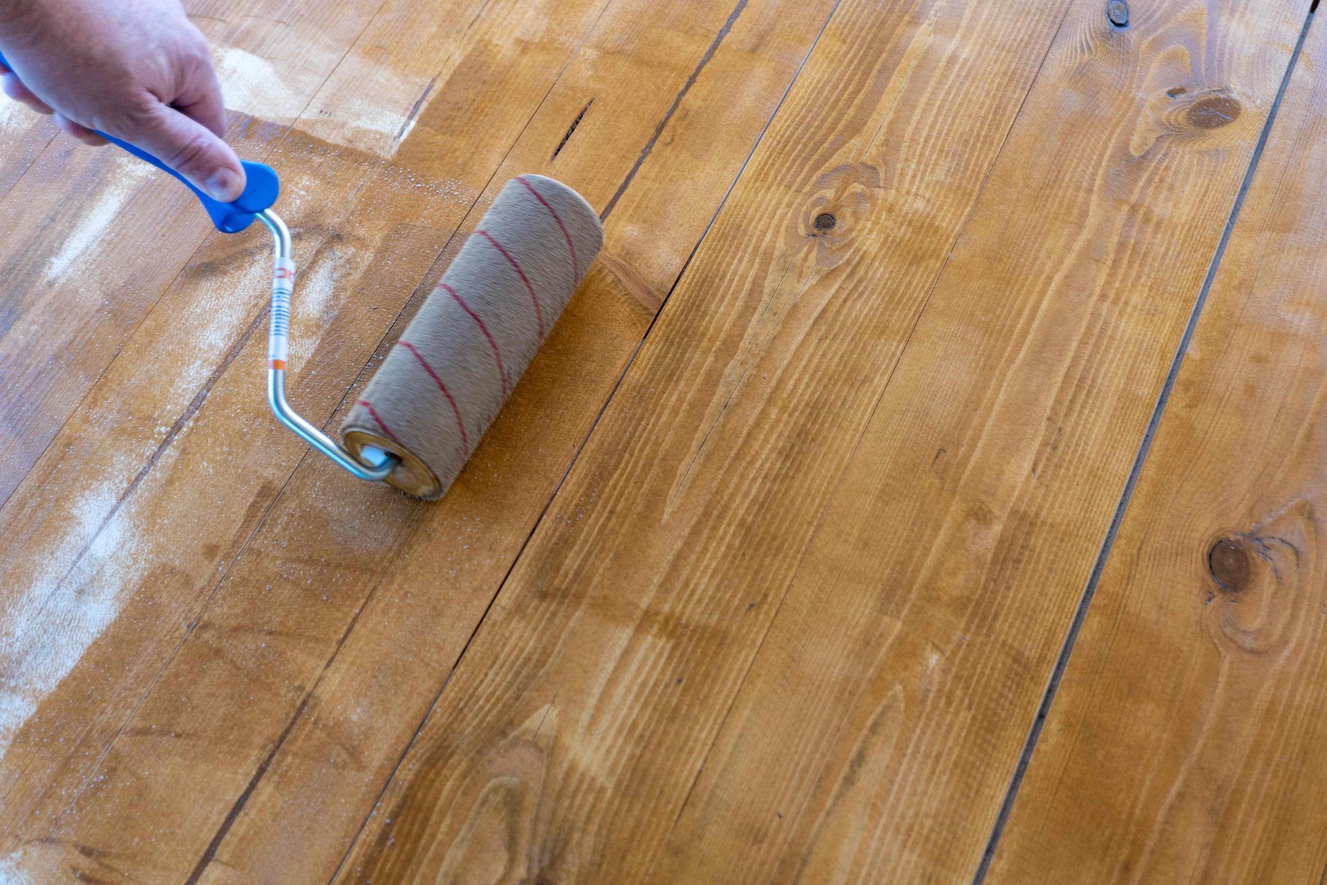 Hand using a blue-handled lint roller on a hardwood floor