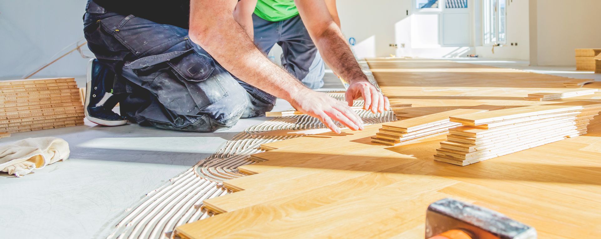 Worker installing wood flooring planks over adhesive during floor renovation.