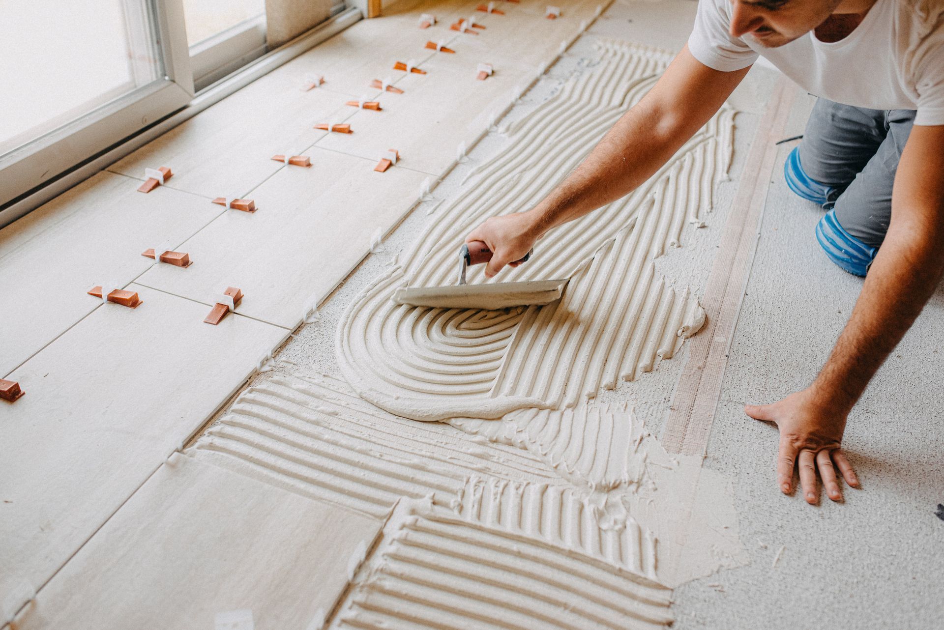 Worker spreading adhesive with a trowel on a floor underlayment during tile installation