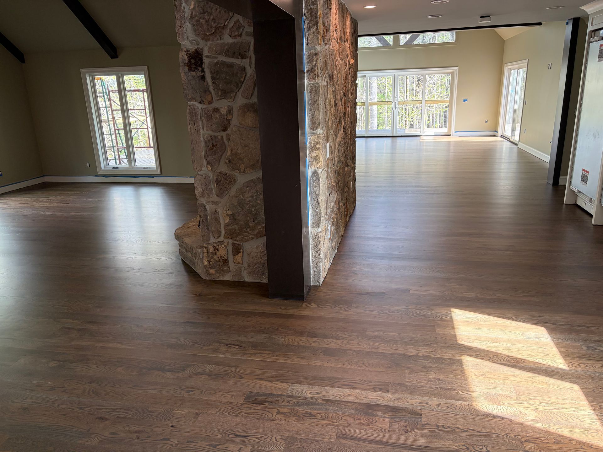 Empty living room with hardwood floors, stone pillar, and large windows letting in sunlight