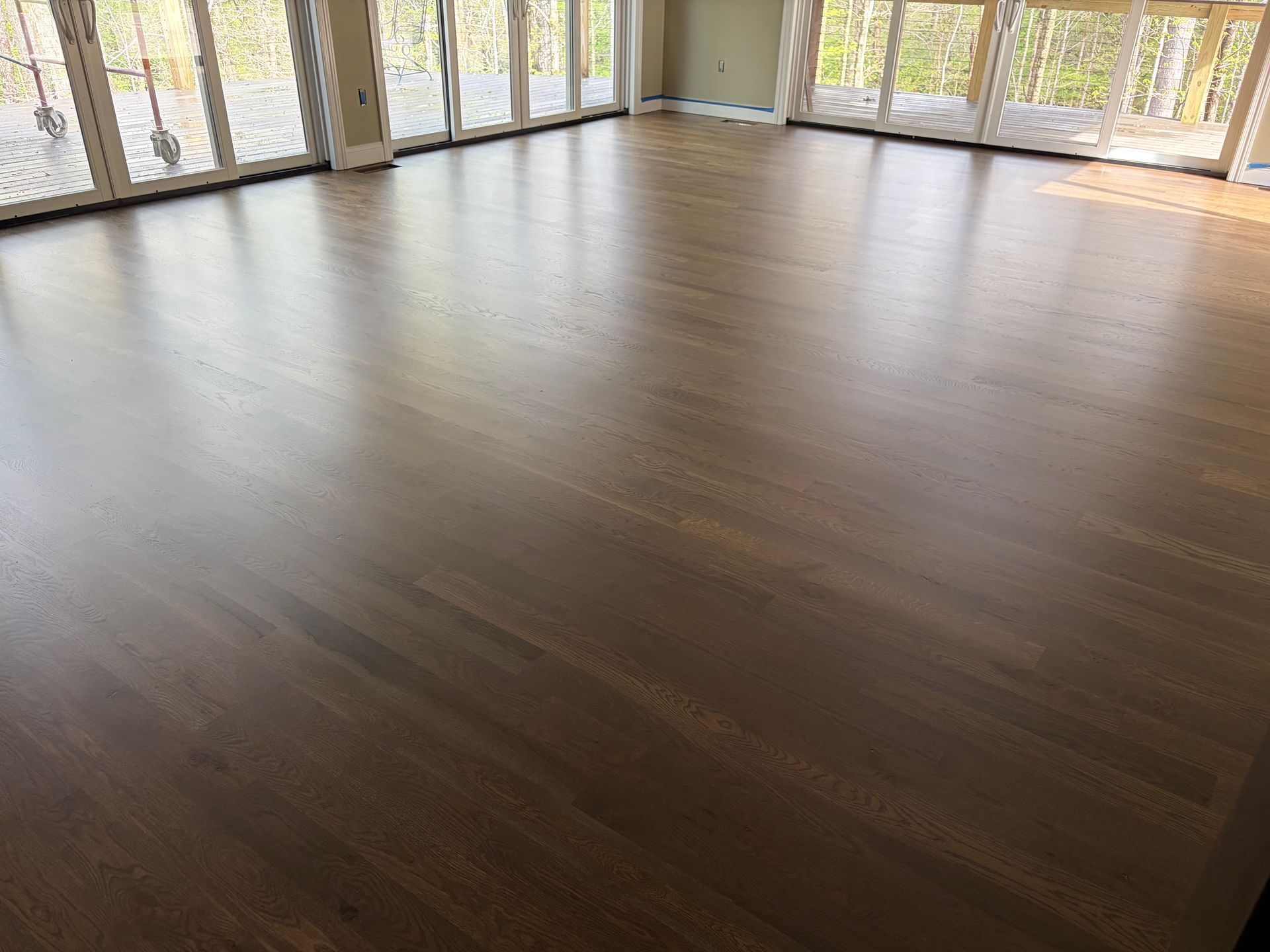 Empty room with polished dark wood floor and floor-to-ceiling windows overlooking trees
