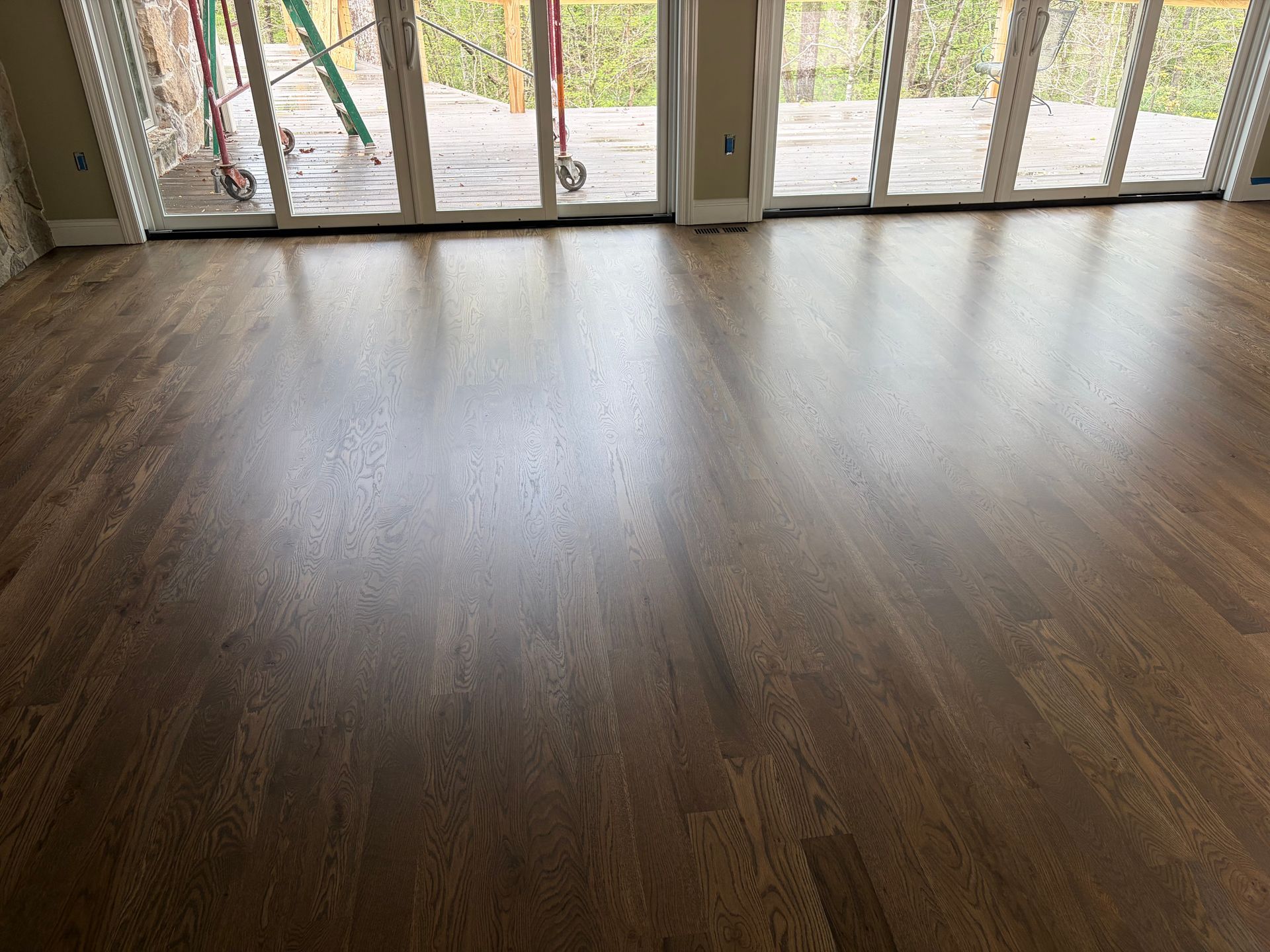 Empty room with dark wood flooring and large glass doors opening to a patio and yard.