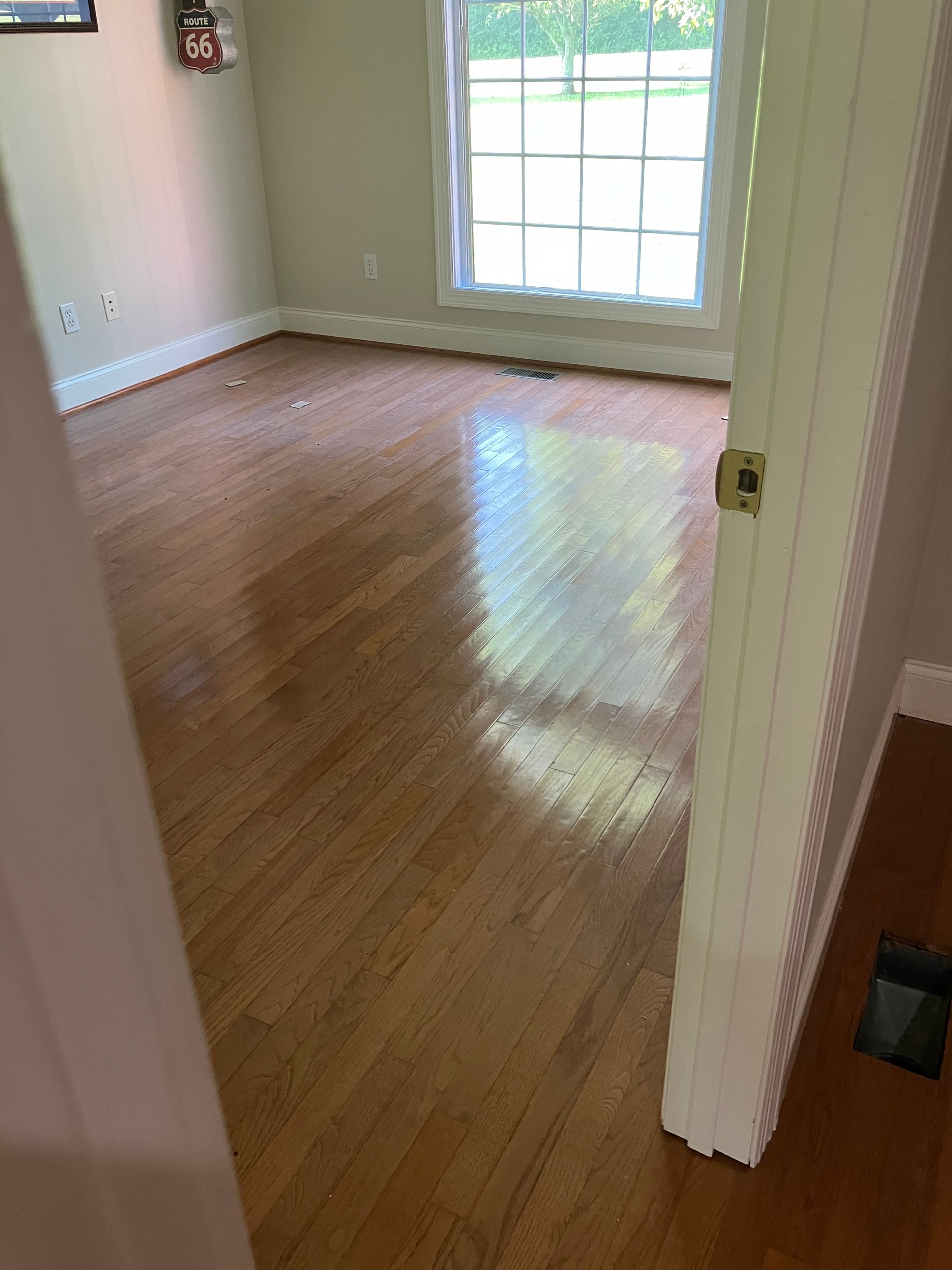 Empty beige room with hardwood floors and a large window letting in sunlight.
