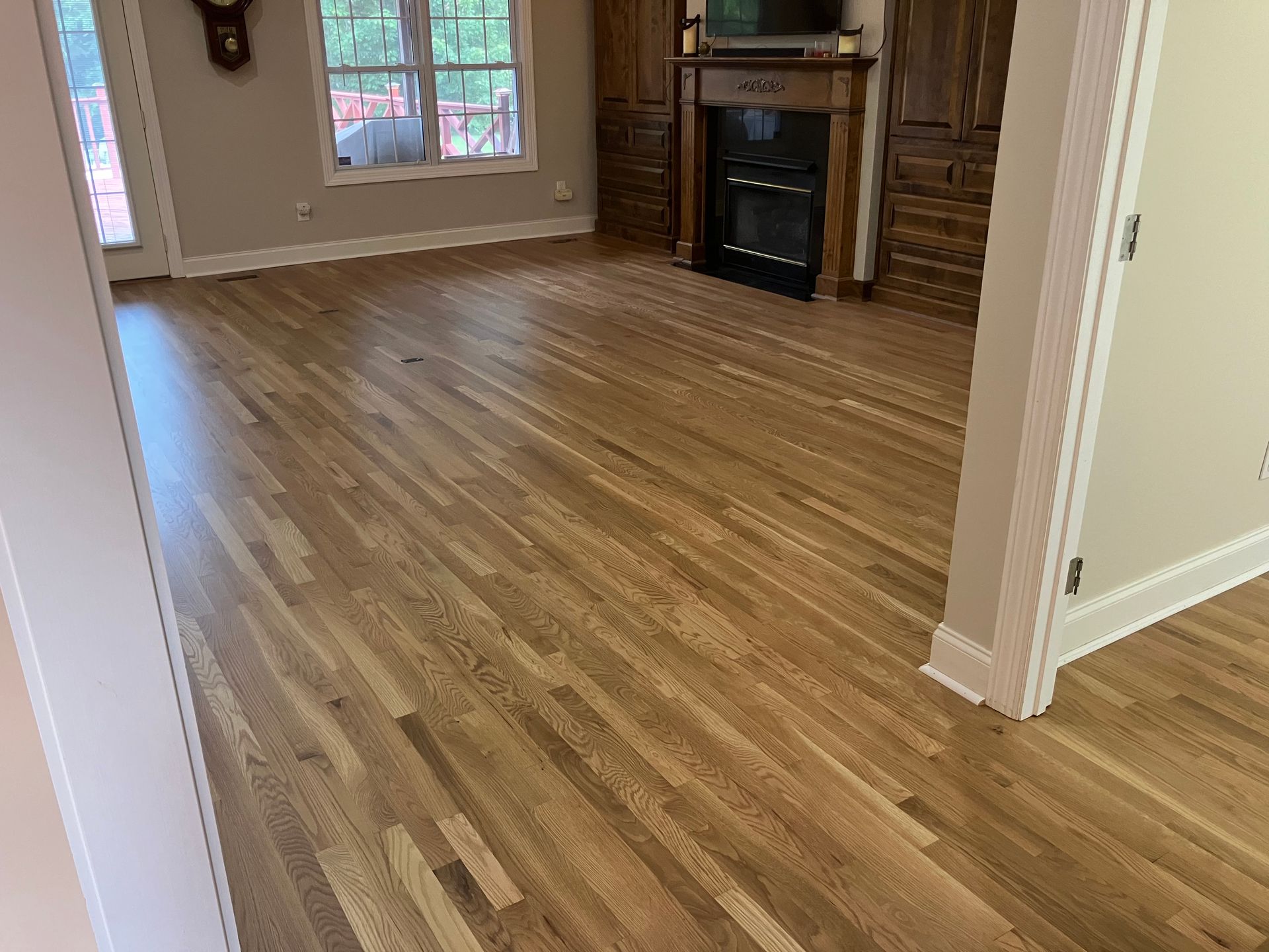 Empty living room with wood flooring, beige walls, and a fireplace near glass doors.