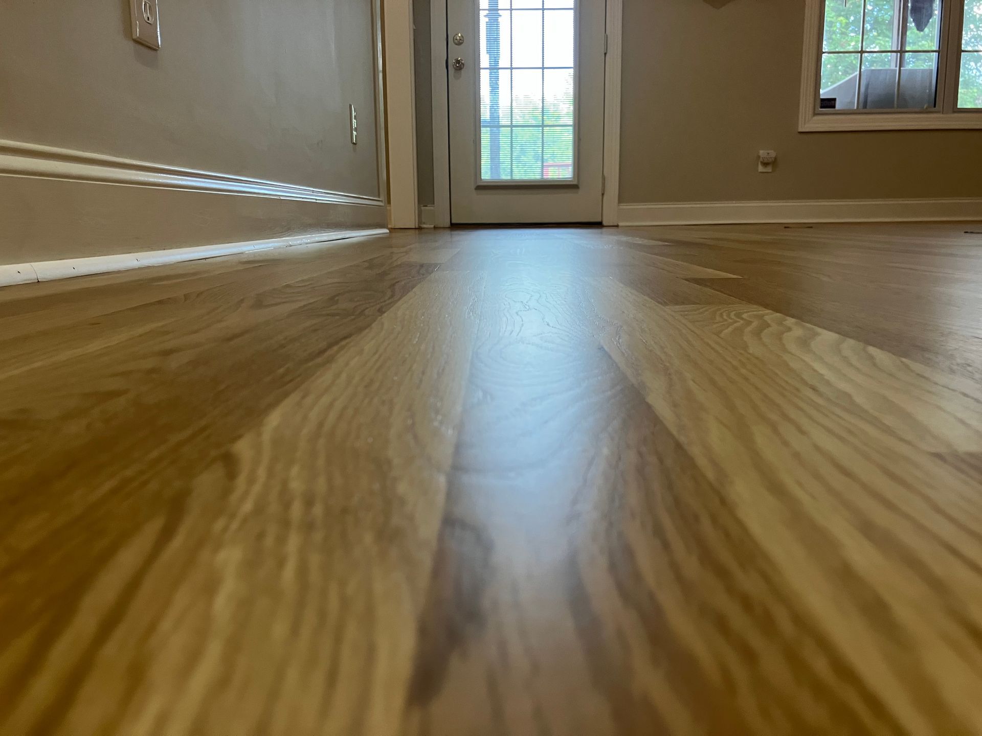 Low-angle view of a hardwood floor leading to a bright doorway and windows in an empty room