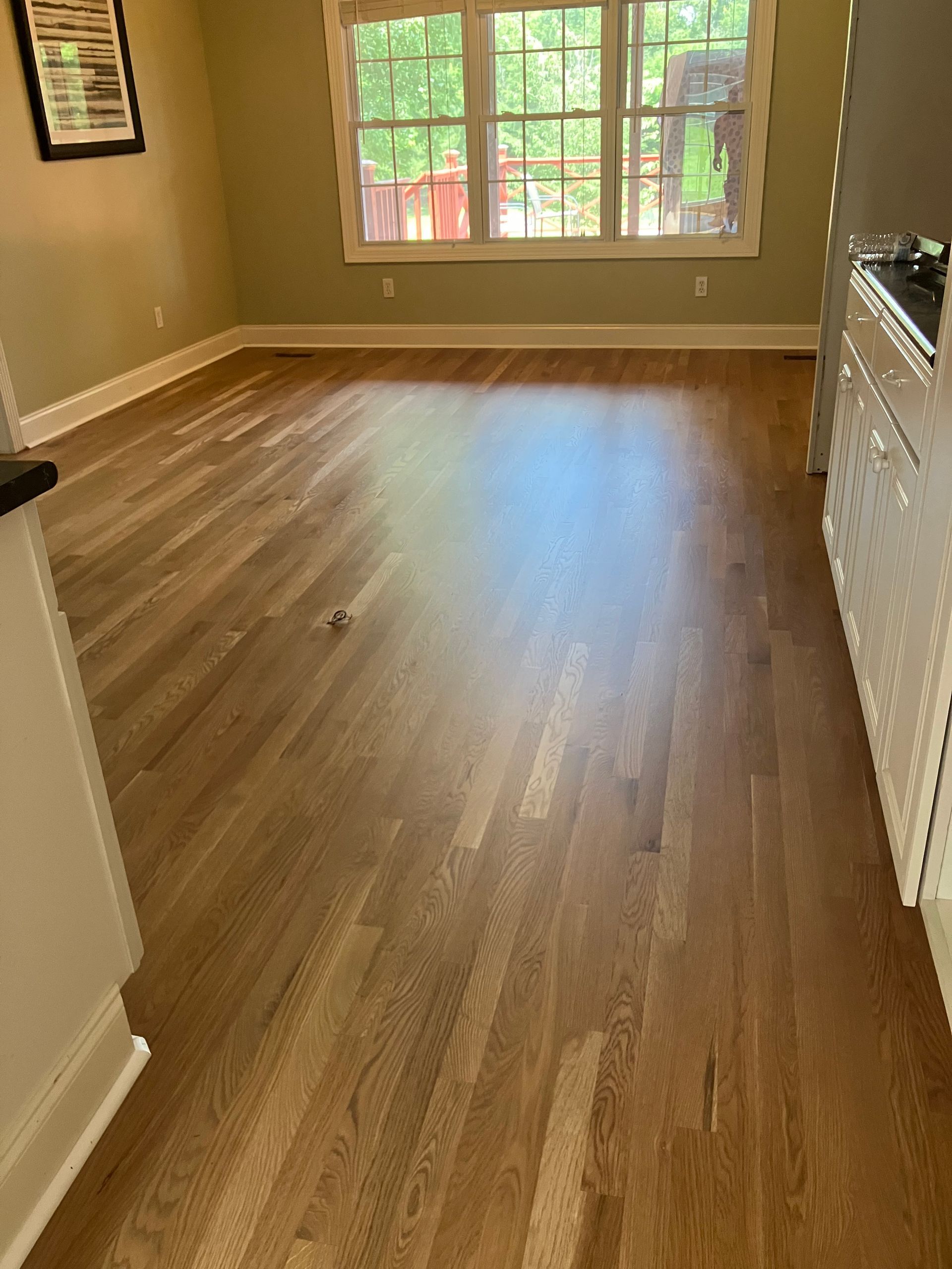 Empty room with wood flooring, beige walls, and a large window letting in daylight.
