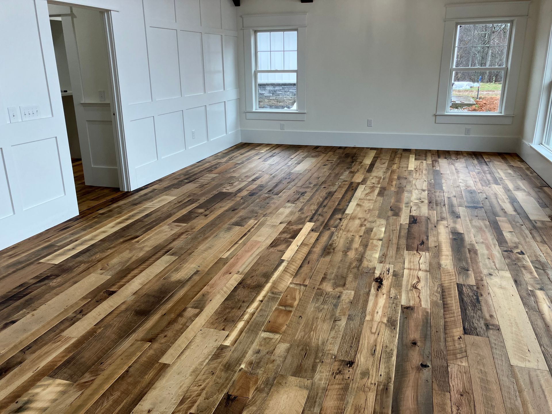 Empty white room with wide plank wooden floor and two windows bringing in natural light