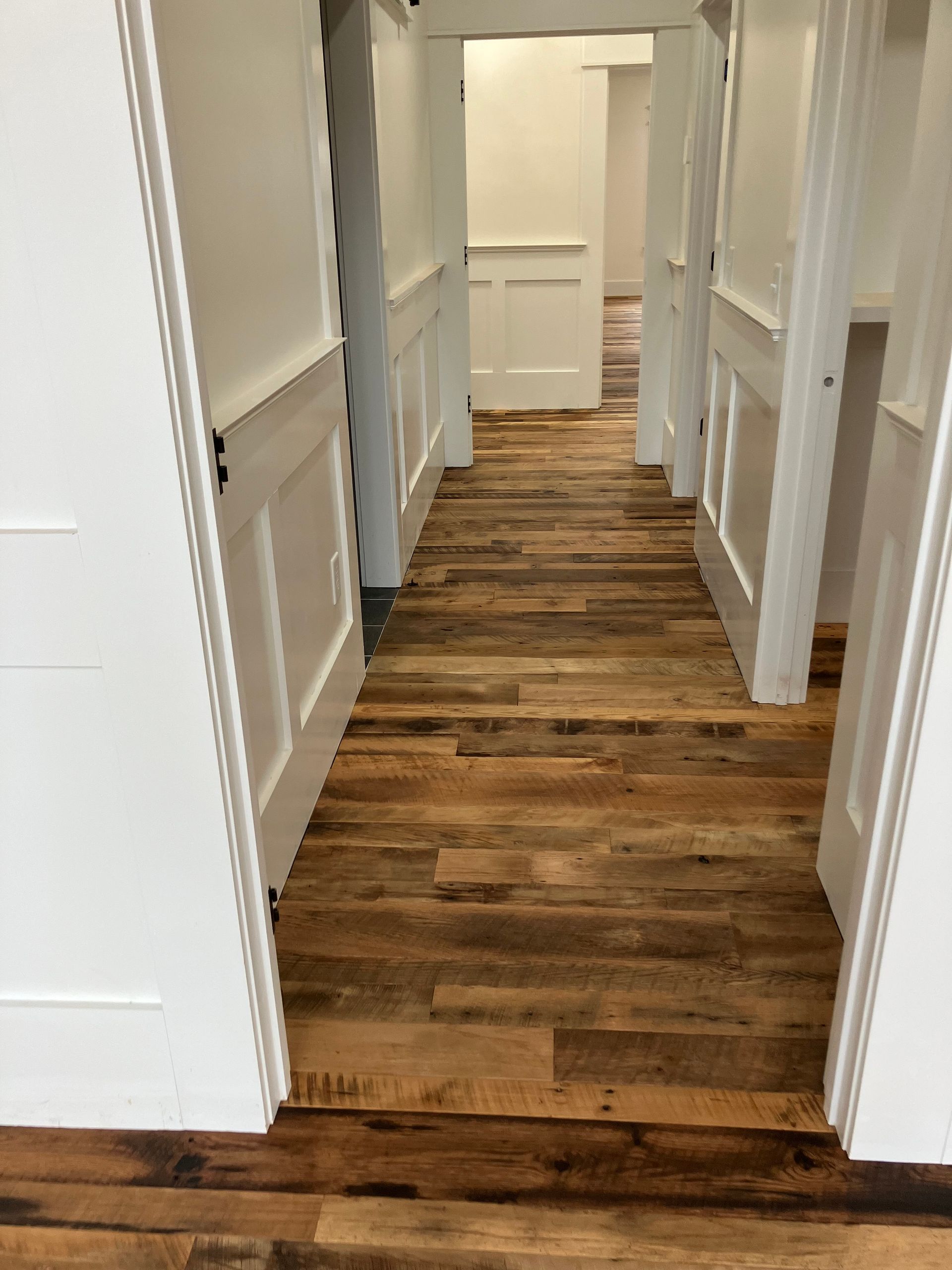 Narrow hallway with wood floor, white walls, and open doorways on both sides.