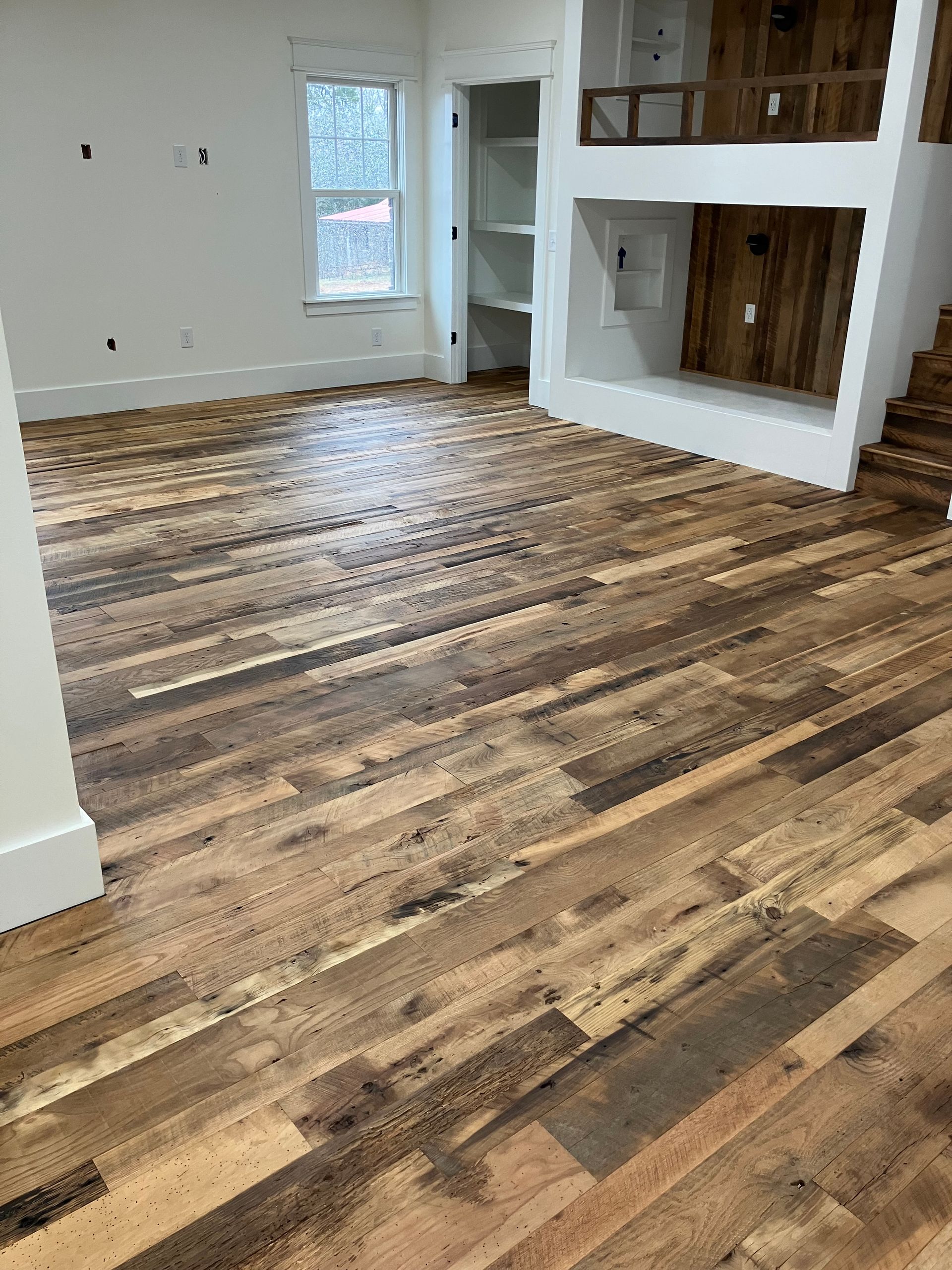 Empty living room with wood plank flooring, white walls, windows, and a built-in fireplace nook